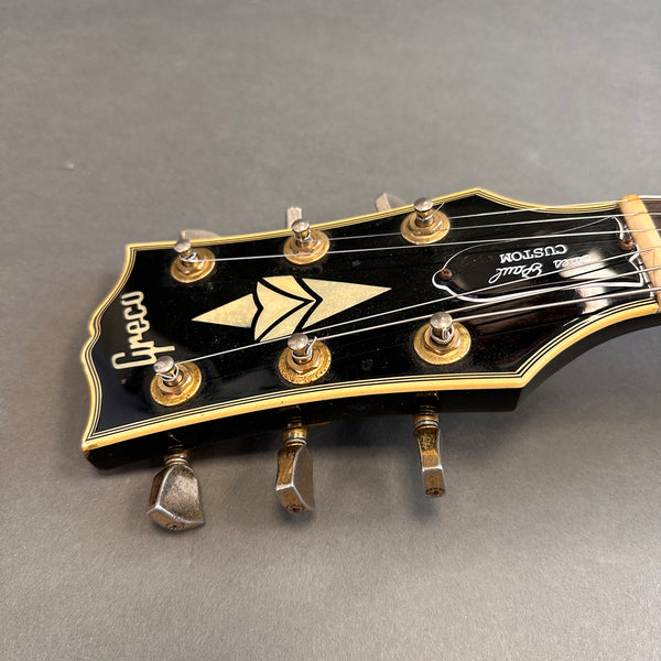 Close-up of vintage Greco guitar headstock with gold tuning pegs and "Super Real Custom" label on black background