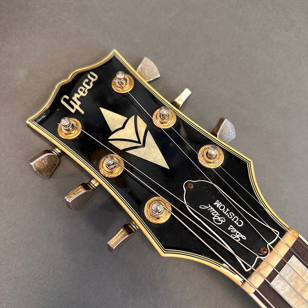 Close-up of Greco Jazz Guitar headstock with vintage tuning pegs and "Real Real Custom" truss cover on gray background