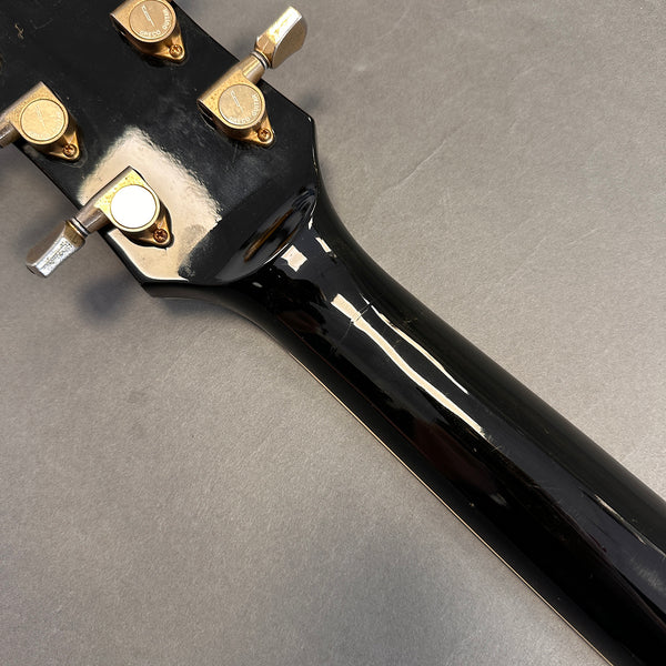 Close-up of black guitar neck and headstock showing gold Greco tuning pegs on a gray background