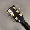 Back of black guitar headstock with six vintage gold tuning pegs labeled "Greco Guitar" and serial number 1861029 on gray background