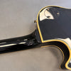 Close-up of black electric guitar body and neck heel with cream binding and control cavity cover on gray background