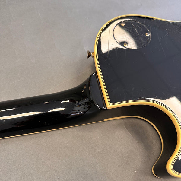 Close-up of black electric guitar body and neck heel with cream binding and control cavity cover on gray background