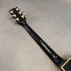 Back view of black guitar neck with six gold tuning pegs on gray background