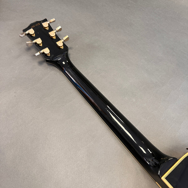 Back view of black guitar neck with six gold tuning pegs on gray background