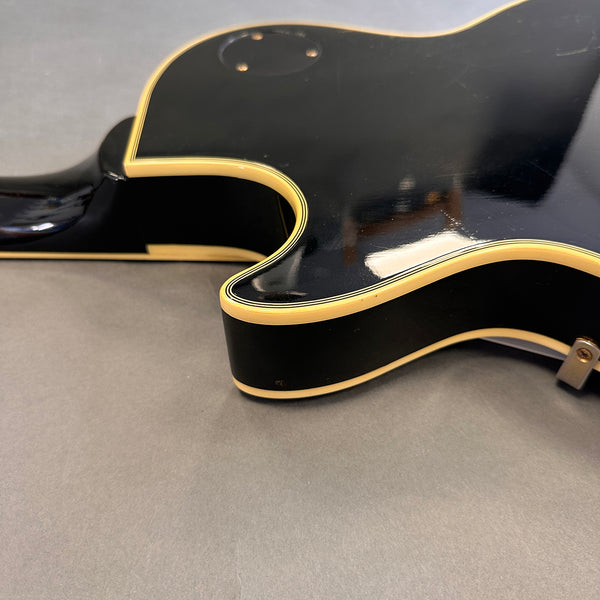 Close-up of black electric guitar body with cream binding and glossy finish on gray background