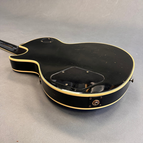 Black electric guitar back with cream binding and rear control cavity on gray surface