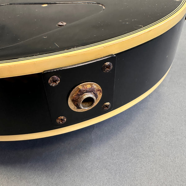 Close-up of rusty output jack and mounting screws on black acoustic guitar with cream binding showing wear and aging details on guitar body