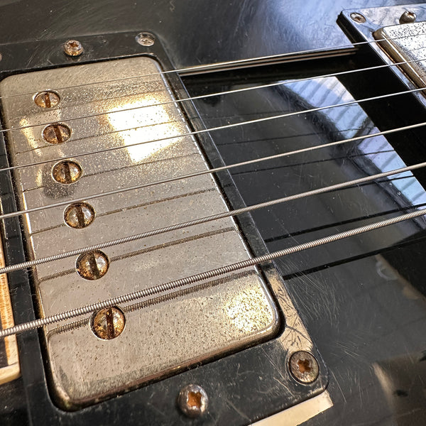 Close-up of vintage electric guitar pickup with rusted screws and guitar strings on black guitar body