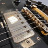 Close-up of vintage electric guitar pickup and bridge showing aged metal with rust and corrosion, black guitar body with control knobs and screws, detailed guitar strings and hardware.