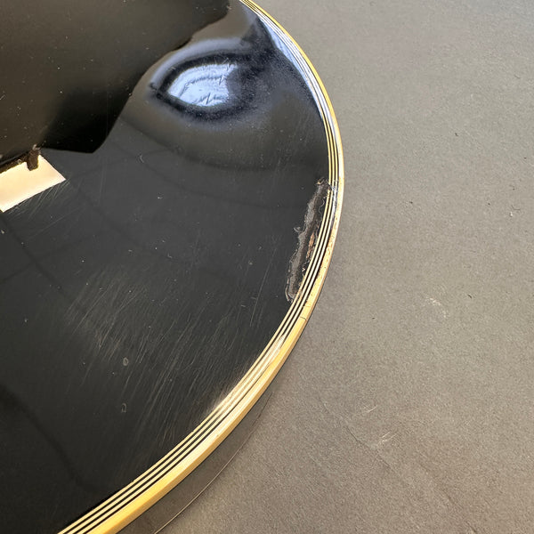 Close-up of black guitar body showing wear and damage near the edge with multi-line cream binding detail