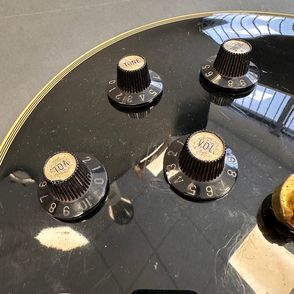 Close-up of black electric guitar control knobs for volume and tone on a glossy black body with white binding trim and visible wear marks