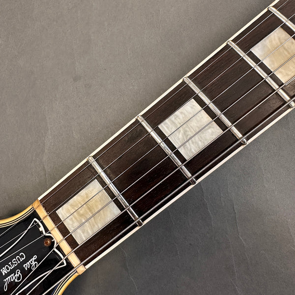 Close-up of a Les Paul Custom guitar rosewood fretboard with mother-of-pearl block inlays and steel strings on a gray background