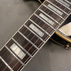 Close-up of guitar fretboard with rectangular pearl inlays and steel strings on a dark wood neck, part of an electric guitar body with cream binding and black finish visible