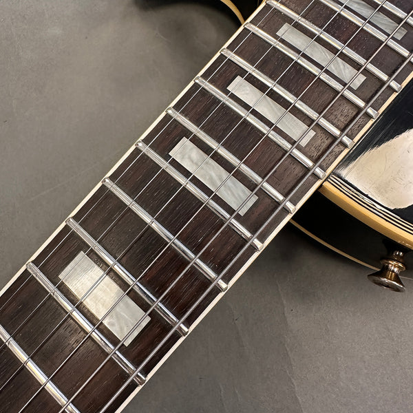 Close-up of guitar fretboard with rectangular pearl inlays and steel strings on a dark wood neck, part of an electric guitar body with cream binding and black finish visible