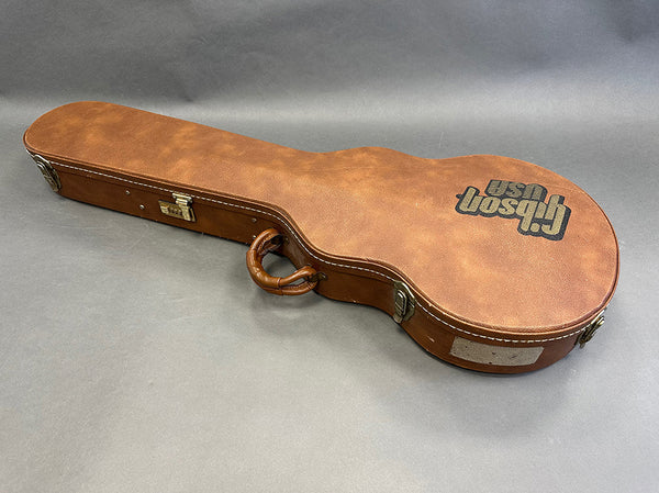 Gibson USA brown hard shell guitar case with leather handle and metal latches on gray background