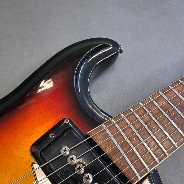 Close-up of sunburst electric guitar body and fretboard with worn metal strings and pickups on gray background