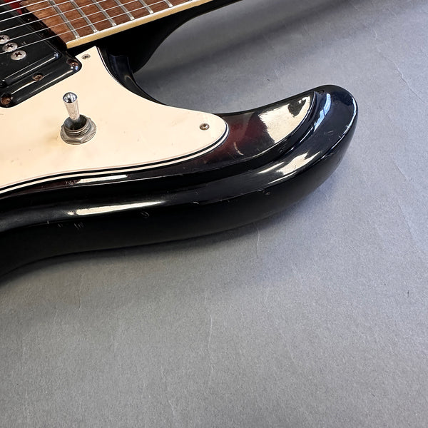 Close-up of black electric guitar body with white pickguard and metal toggle switch on gray surface