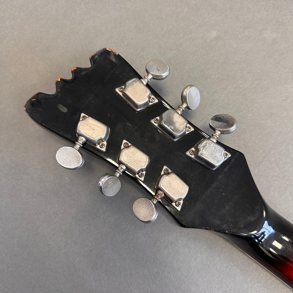 Close-up of worn black guitar headstock with six silver tuning pegs on gray background