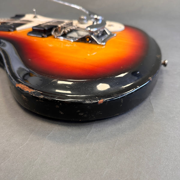 Close-up of sunburst electric guitar body showing worn black edges and scratch details on gray surface background