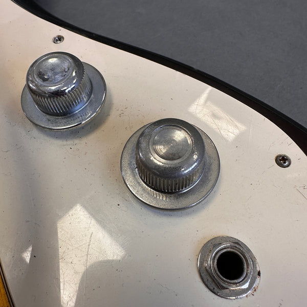 Close-up of vintage electric guitar volume and tone control knobs with output jack on white pickguard showing wear and scratches