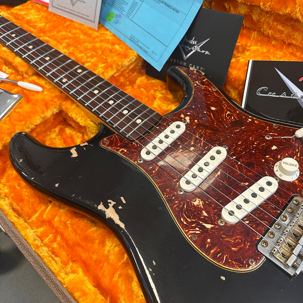 Vintage black electric guitar with tortoiseshell pickguard and three single-coil pickups in orange plush-lined case with Fender custom case documentation