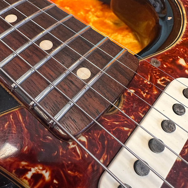 Close-up of electric guitar fretboard and strings with tortoiseshell pickguard and vintage single-coil pickups