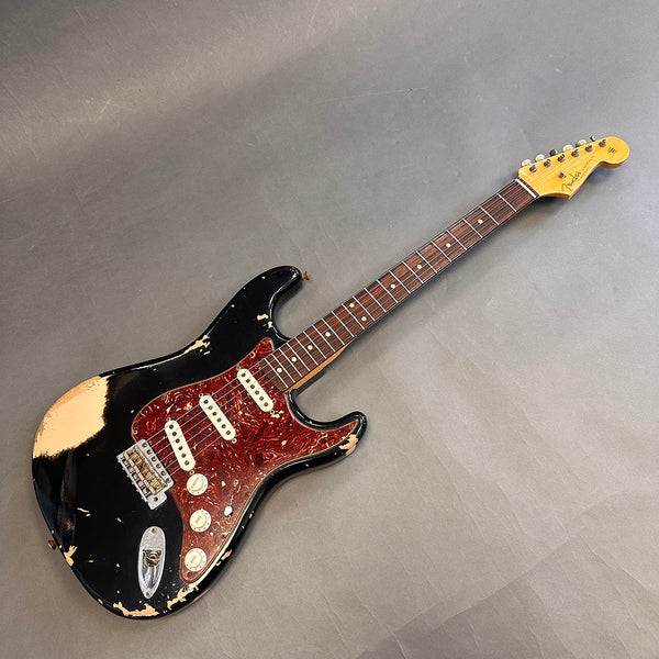 Vintage Fender Stratocaster electric guitar with black worn finish, tortoiseshell pickguard, and maple neck with rosewood fingerboard