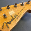 Close-up of vintage Fender Stratocaster headstock with tuning pegs and strings on natural wood finish guitar neck showing Fender logo and "With Synchronized Tremolo" text