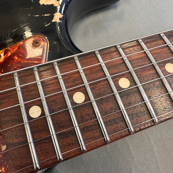 Close-up of electric guitar fretboard with metal frets, dot inlays, and worn black body showing chipped paint near pickguard.