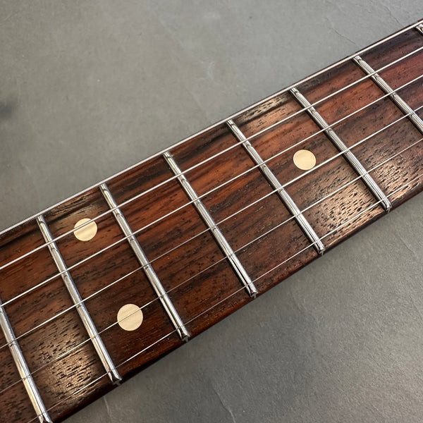 Close-up of rosewood guitar fretboard with dot inlays and metal frets on gray background