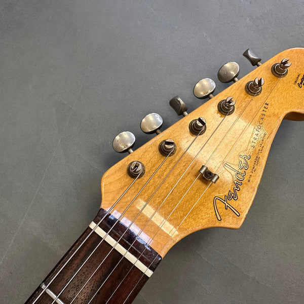 Close-up of Fender Stratocaster guitar headstock with vintage tuning pegs and rosewood fretboard on gray background