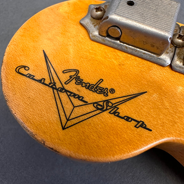 Close-up of Fender Custom Shop logo on natural wood finish guitar body with metal bridge plate and screws