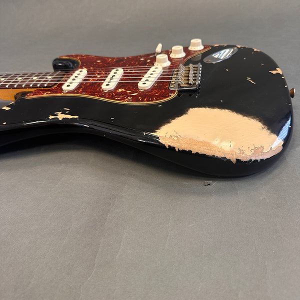 Close-up of black electric guitar with heavy wear and tortoiseshell pickguard, showing vintage-style pickups and control knobs on gray background