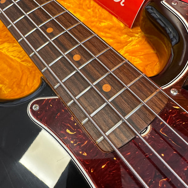 Close-up of four-string electric bass guitar fretboard and tortoiseshell pickguard on black body with yellow case lining background