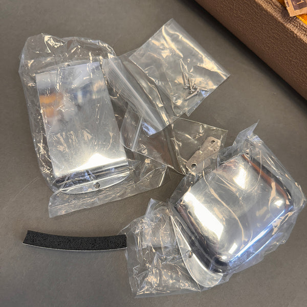 Chrome guitar bridge and pickup covers with mounting screws and foam padding on gray surface from Coffee House Guitars