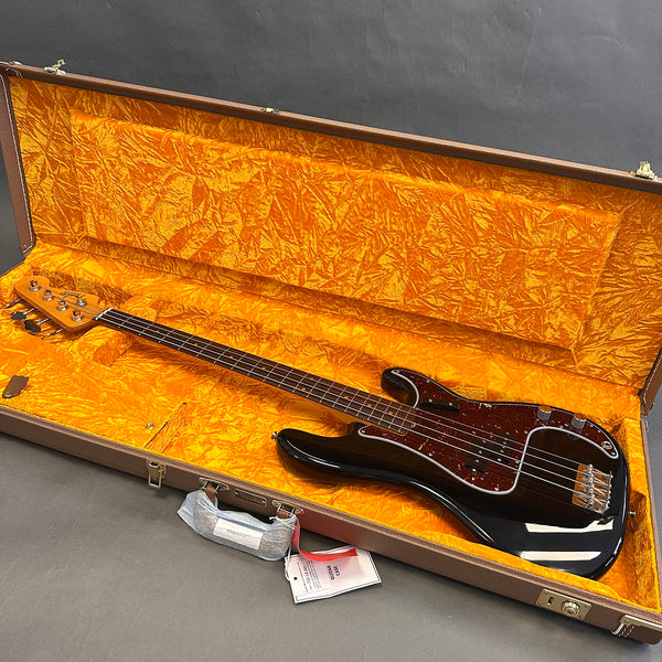 Black Fender Precision bass guitar with tortoiseshell pickguard in open brown hard case lined with bright orange plush interior
