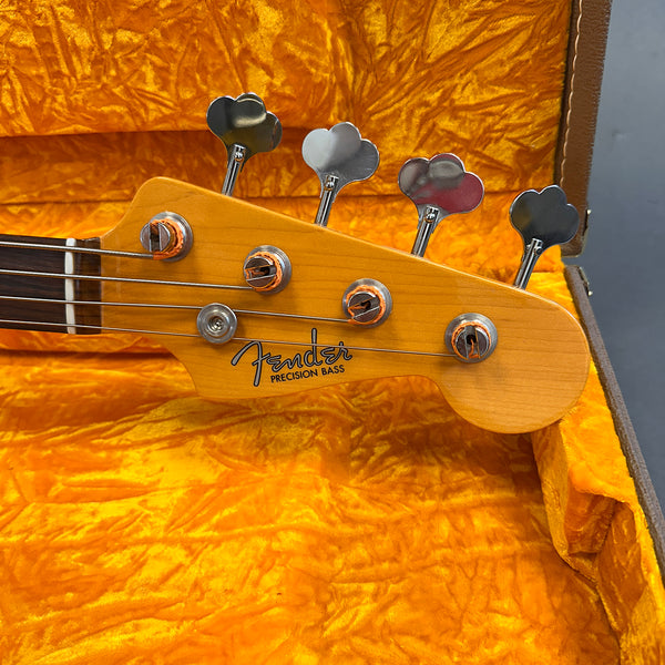 Close-up of Fender Precision Bass headstock with tuning pegs and strings inside vintage orange plush guitar case
