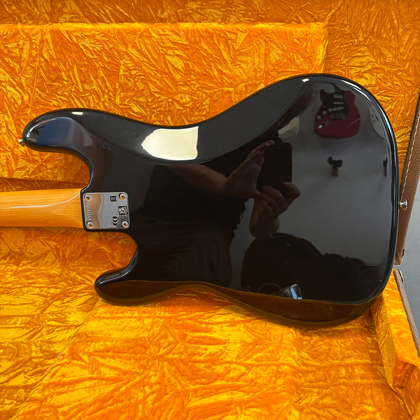 Glossy black electric guitar body with maple neck and four-screw neck plate inside bright orange textured guitar case interior