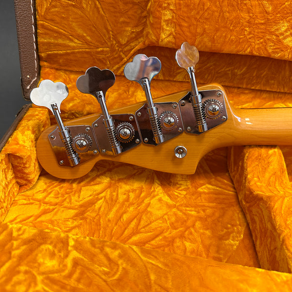 Close-up view of maple wood bass guitar headstock with vintage chrome tuning pegs inside orange plush-lined hard case