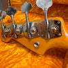 Close-up of tuning machines on the headstock of a natural wood electric bass guitar resting on orange plush fabric case lining