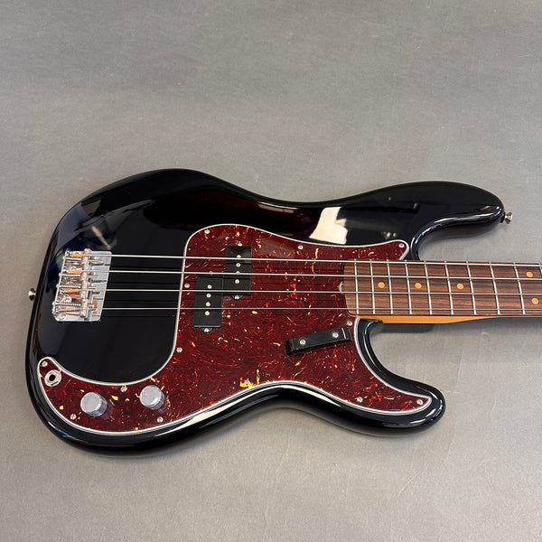 Black electric bass guitar with tortoiseshell pickguard and rosewood fretboard on gray background