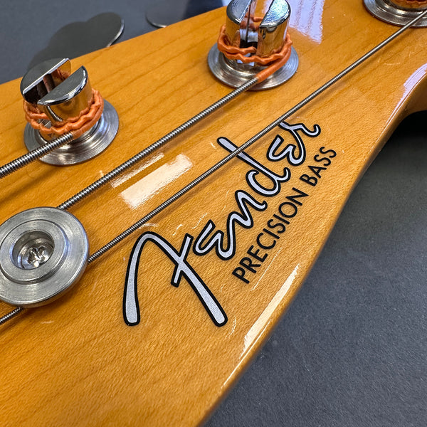 Close-up of Fender Precision Bass headstock with tuning pegs and strings on natural wood finish