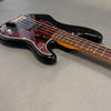Close-up angled view of black electric bass guitar with tortoiseshell pickguard and rosewood fingerboard on gray surface