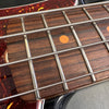 Close-up of bass guitar fretboard showing metal frets, round orange fret markers, and wrapped metal strings on dark wood fingerboard with tortoiseshell pickguard edge.