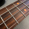 Close-up of bass guitar fretboard with metal frets, wound strings, and dot inlays on dark wooden fingerboard