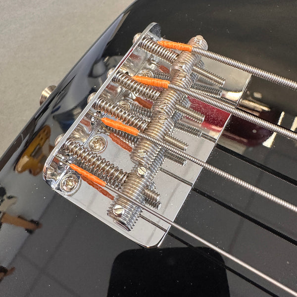 Close-up of chrome bridge and saddle with wrapped strings on black electric bass guitar