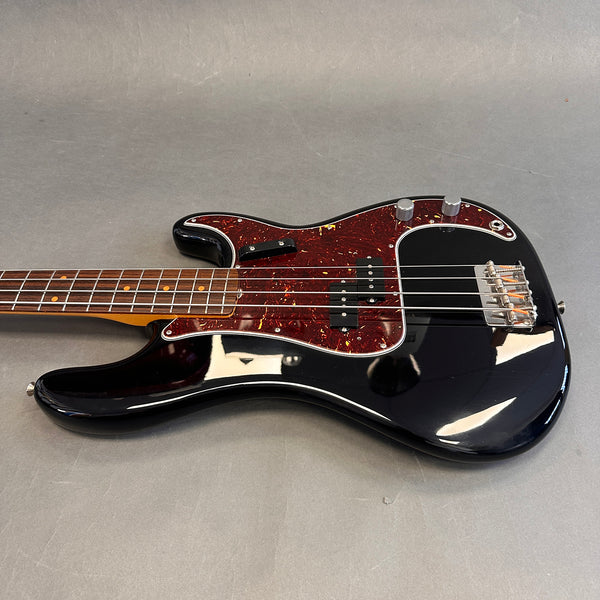 Black electric bass guitar with tortoiseshell pickguard and rosewood fretboard on gray background
