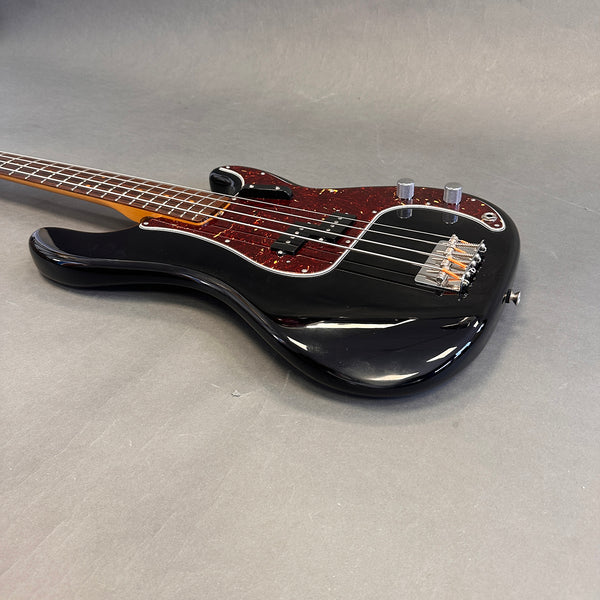 Black electric bass guitar with tortoiseshell pickguard and chrome knobs on gray background