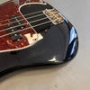 Close-up of black electric bass guitar body with tortoiseshell pickguard and metal bridge on gray surface
