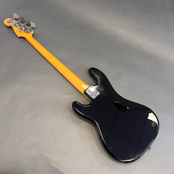 Black electric bass guitar with maple neck and chrome tuning pegs shown from the back on gray background